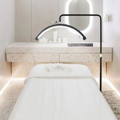 a white bed sitting under a bathroom mirror next to a counter with a light on it