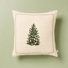 a green pillow with a small pine tree on the front and side, against a pale green wall