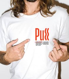 a man with long hair wearing a white t - shirt and pointing at the camera