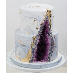 a three tiered cake decorated with gold and purple marbles on a white pedestal