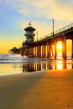 the sun is setting behind a pier at the beach