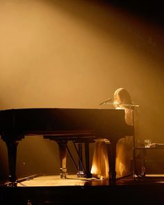 a woman sitting at a piano in front of a microphone on stage with lights behind her