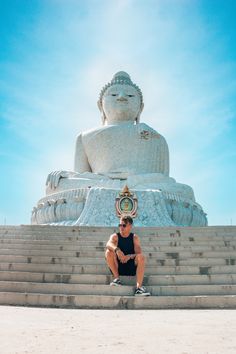 a person sitting on some steps in front of a big buddha statue