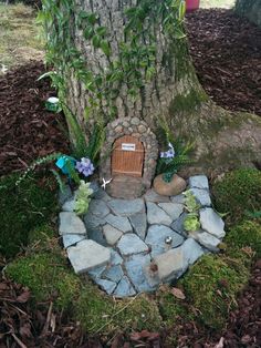 a tree with a small door in the ground next to a rock path and a potted plant