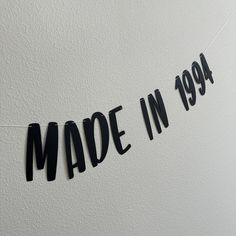 the word made in 1994 is cut out from black paper and hung on a white wall