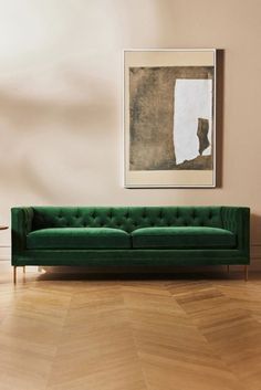 a green couch sitting on top of a hard wood floor next to a framed painting