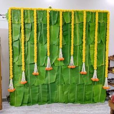 a wall made out of green leaves with yellow flowers hanging from the sides and beads on each side