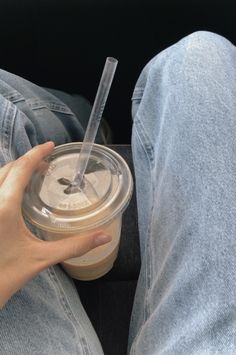 a person sitting down holding a cup with a straw in it and the lid open