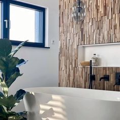 a white bath tub sitting under a window next to a plant in a vase on top of a counter