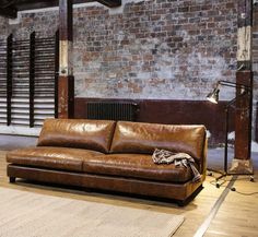 a brown leather couch sitting on top of a wooden floor next to a brick wall