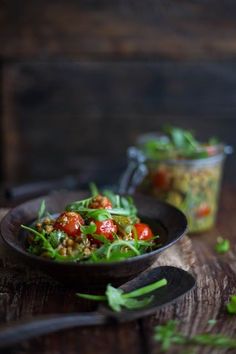 a bowl filled with salad sitting on top of a wooden table next to a spoon