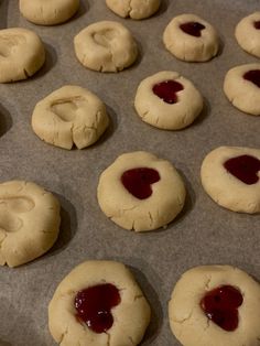 several cookies with jam on them sitting on a baking sheet, ready to go into the oven