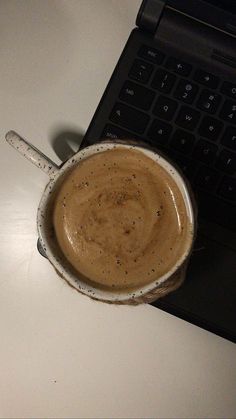 a cup of coffee sitting on top of a white table next to a laptop computer