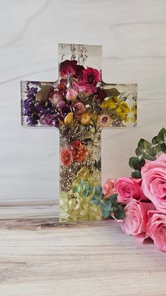 a cross made out of flowers sitting on top of a table next to a vase