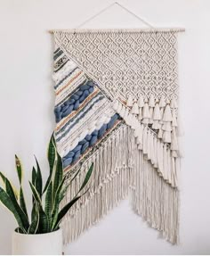 a plant in a white vase next to a macrame wall hanging