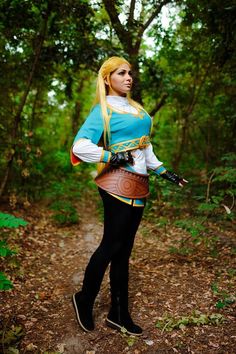 a woman dressed in a costume standing on a dirt path surrounded by trees and leaves