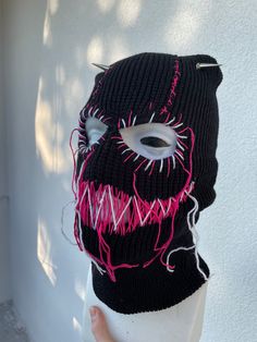 a knitted mask with pink and white lines on it's face is hanging up against a wall