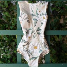 a white bodysuit with flowers on it hanging from a green fence in front of greenery