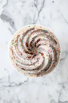 a cupcake topped with white frosting and sprinkles on a marble surface