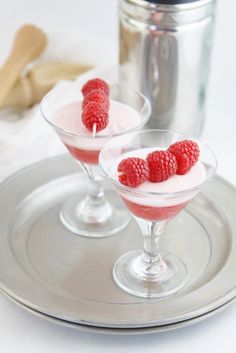 two desserts with raspberries in small glasses on a silver tray next to a canister