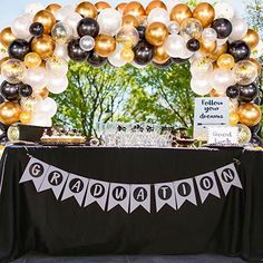 an arch made out of balloons and streamers with graduation decorations on the front table