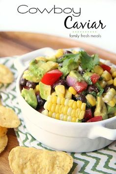 a white bowl filled with corn, black beans and avocado salsa next to tortilla chips