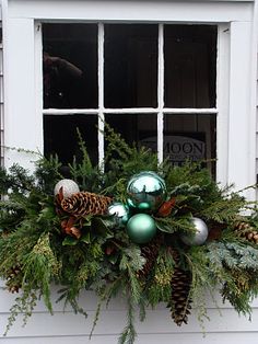 a window sill decorated with evergreen, pine cones and baubes in front of a white house