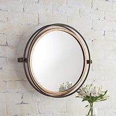 a round mirror hanging on the wall next to a vase with flowers