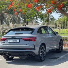 the rear end of an audi suv parked in a parking lot with trees and flowers behind it