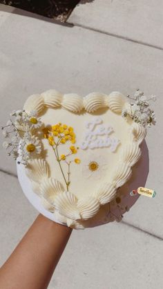 someone holding a heart shaped cake with flowers on it