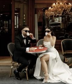 a man and woman are sitting at a table drinking coffee while the lady is dressed in a white dress