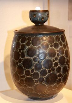 a brown and black vase sitting on top of a white table next to a wall