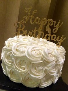 a birthday cake with white frosting and gold letters on top, sitting on a table