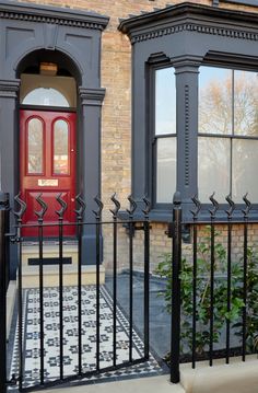 a red door sits in front of a black iron fence and brick building with two windows