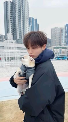 a young man holding a small dog in his arms while wearing a jacket and scarf