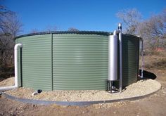 a large green water tank sitting on top of a dirt field