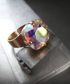 Full of iridescent shimmer & sparkle! Renowned for impeccable faceting and quality, this 'Crystal AB' Swarovski crystal flashes playfully with soft, pastel hues in all hues of the rainbow! The square cushion-cut crystal is set into a matte, soft gold-plated bezel on an adjustable ring band. Fits sizes approx. 6 to 9 (may not fit smaller fingers). Also available with Antiqued Silver adjustable ring band - sold separately. Cushion-cut Swarovski crystal: 1/2" x 1/2" (12 x 12mm) Comfortable and Beautiful Promise Rings, Swarovski Crystal Rings, Small Skull, Sparkling Rings, Crystal Ab, Drop Necklace, Crystal Rings, Matte Gold, Adjustable Rings