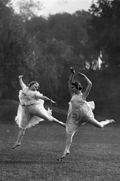 two women in dresses are dancing on the grass