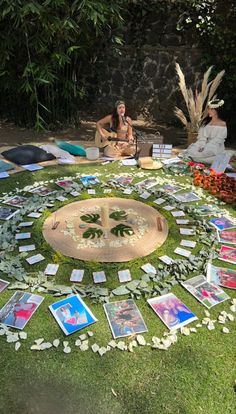 two people sitting on the grass in front of a circular table with pictures and flowers