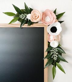 a blackboard with flowers on it and leaves around the edges is displayed in front of a white wall