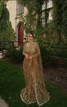 a woman standing in front of a building wearing a gold dress with sequins on it