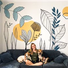 a woman sitting on top of a couch with two dogs in front of a wall mural