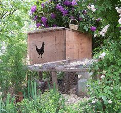 a wooden box with a chicken on it in the middle of some bushes and flowers