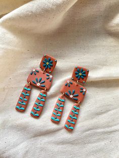 two pairs of pink and blue earrings with flowers on them sitting on a white cloth