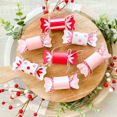 red and white paper wrapped candy on a wooden platter with greenery around it