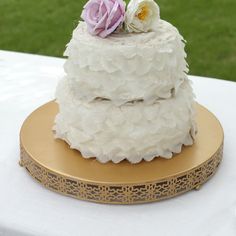 a three tiered cake with white frosting and pink flowers on top sitting on a gold plate