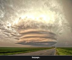 an image of a long road with clouds in the sky and grass on either side