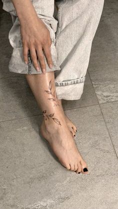 a person sitting on the floor with their foot covered in tattoos and holding onto her leg