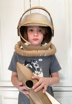 a young boy wearing an astronaut's helmet and holding a piece of brown paper