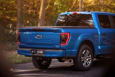 a blue truck is parked on the side of the road in front of some trees